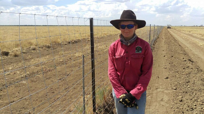 Melinda Driver is wearing sun protection gear and stands next to the wild dog fence she is building.