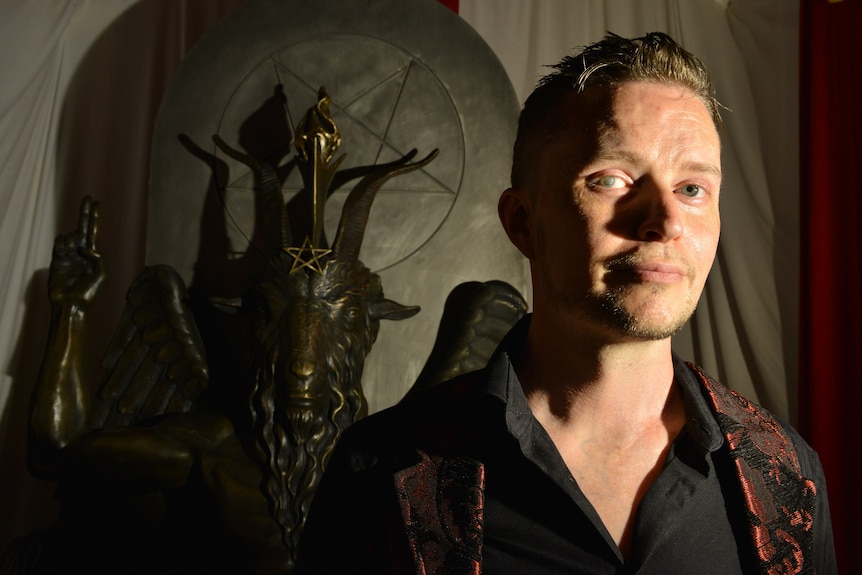 Lucien Greaves inside The Satanic Temple in front of deity statue
