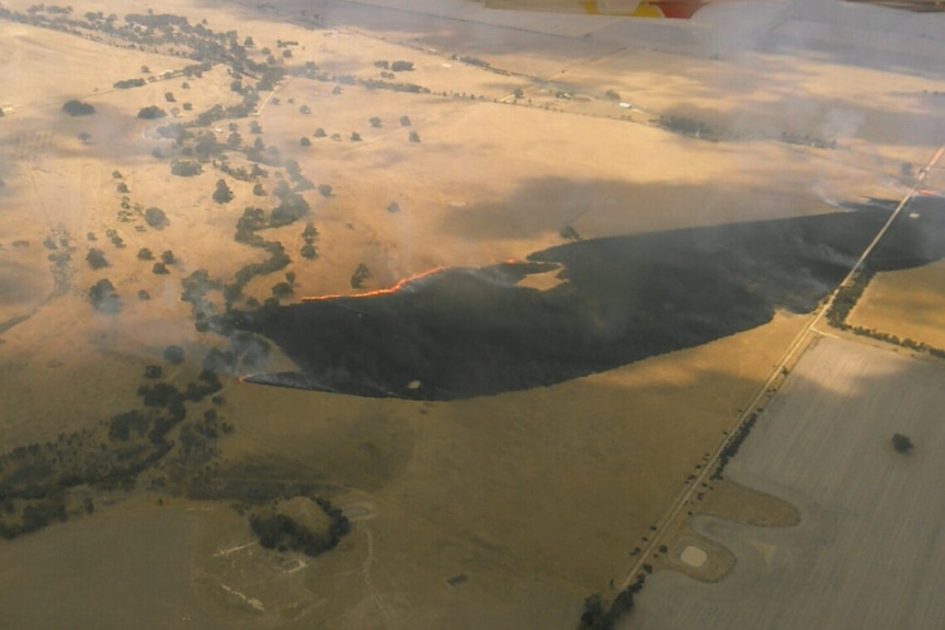 a photo from a plane shows a line of fire and a burnt area in dry paddocks.