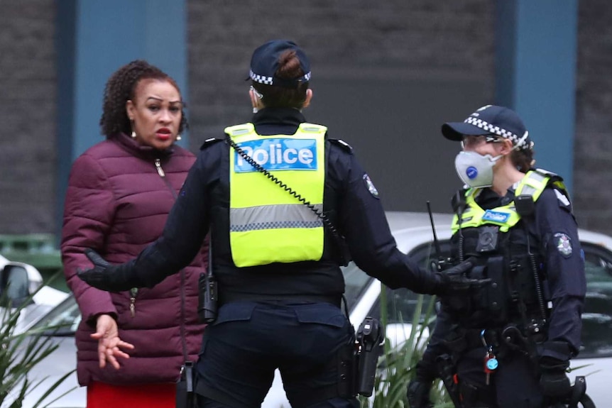 Police wearing masks speak to a woman outside a block of units in Flemington, Melbourne.