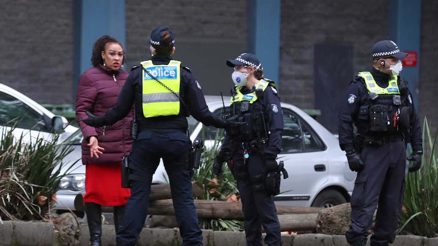 Police wearing masks speak to a woman outside a block of units in Flemington, Melbourne.