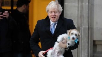 British Prime Minister Boris Johnson wears a suit and carries his dog in his arms.