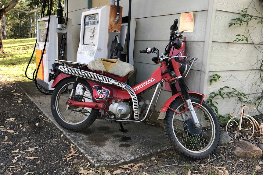 An old red Honda motorcycle leaning up against a wall.