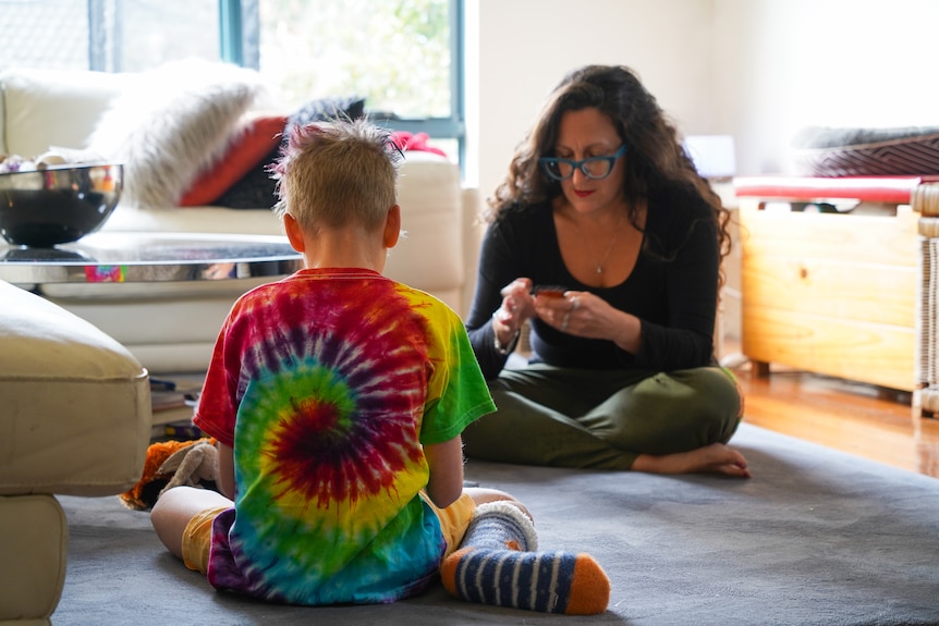 Jenny and her youngest son sit on the lounge room floor playing cards.