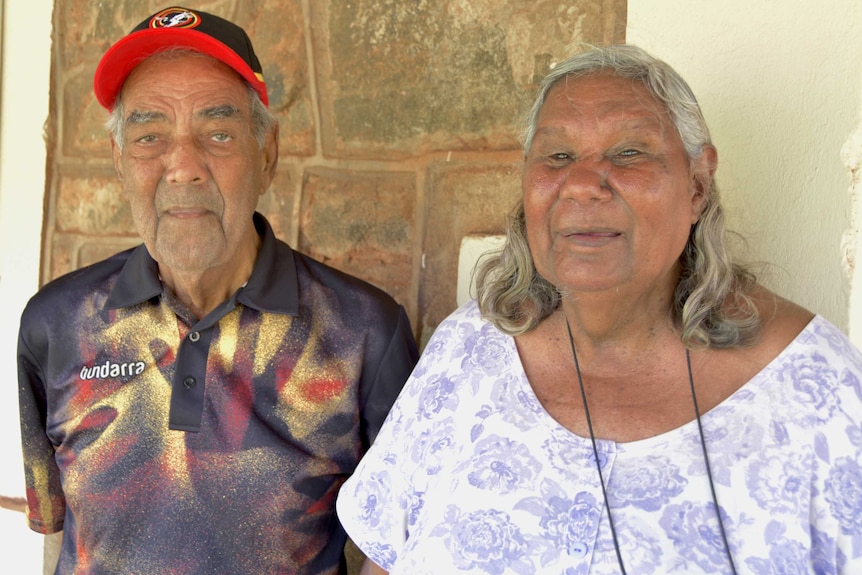 A mid-shot of Ngarluma Aboriginal elders David Walker and Pansy Hicks standing up against a concrete wall.