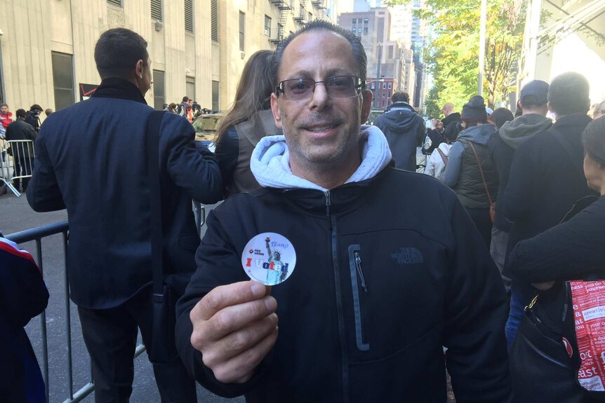 A man in New York holds up an "I voted" sticker with "Trump" handwritten on it.