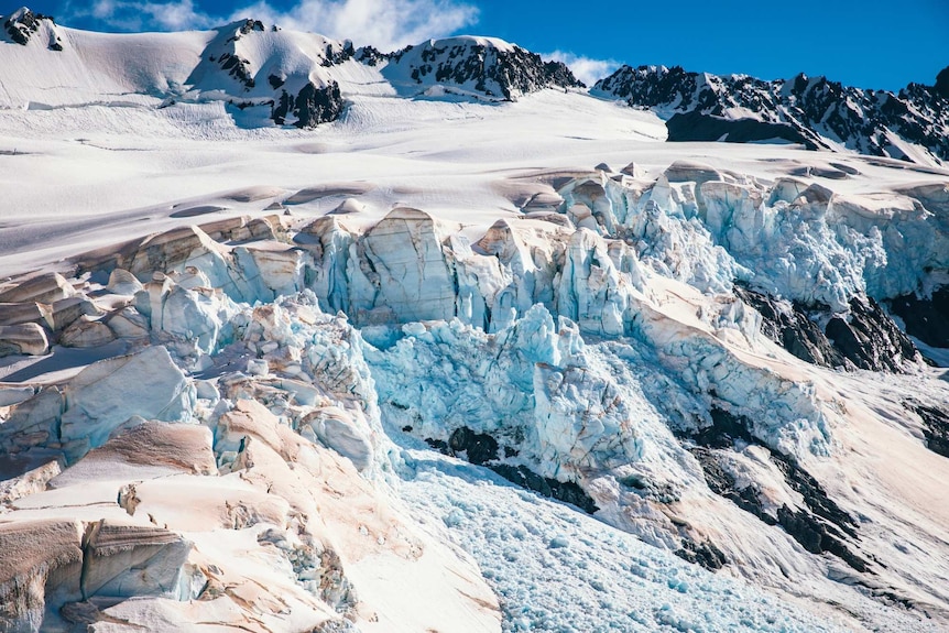 Snow and ice tinged with red cover craggy black rocks.