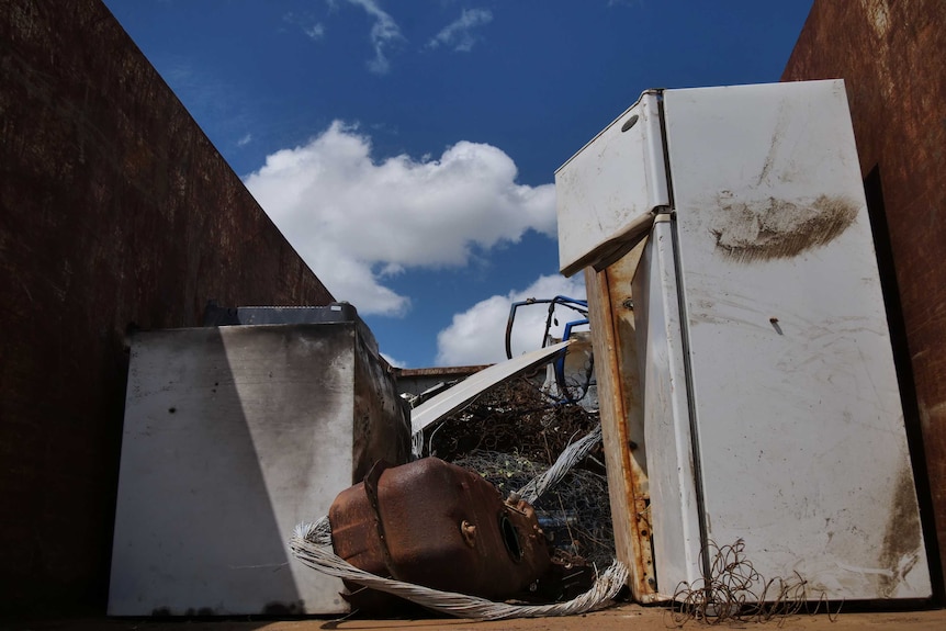 A rusty fridge, washing machine and other metal items inside a big skip bin.
