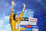 Cate Campbell raises her arms on the podium.