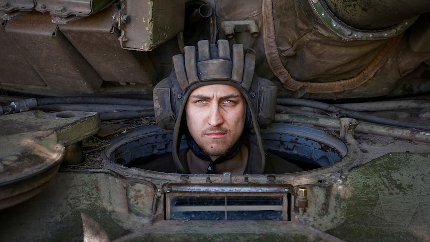 A man in a helmet looks out of a tank, with a fierce expression on his face 