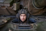 A man in a helmet looks out of a tank, with a fierce expression on his face 