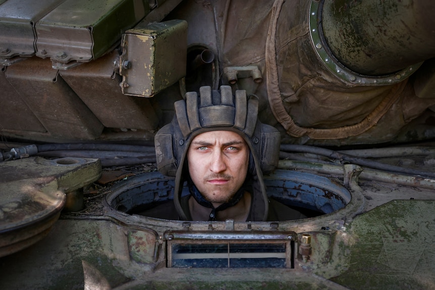 A man in a helmet looks out of a tank, with a fierce expression on his face 