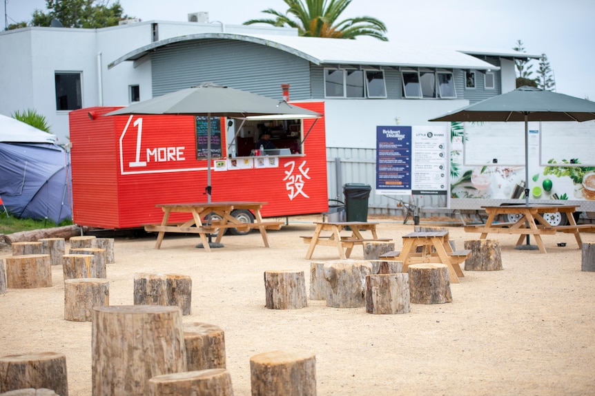 Une camionnette alimentaire rouge, avec des tables de pique-nique en bois vides et des sièges au premier plan