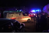 Two ambulances with their lights on drive on a crowded dirt road at night time 