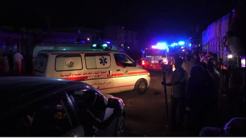 Two ambulances with their lights on drive on a crowded dirt road at night time 