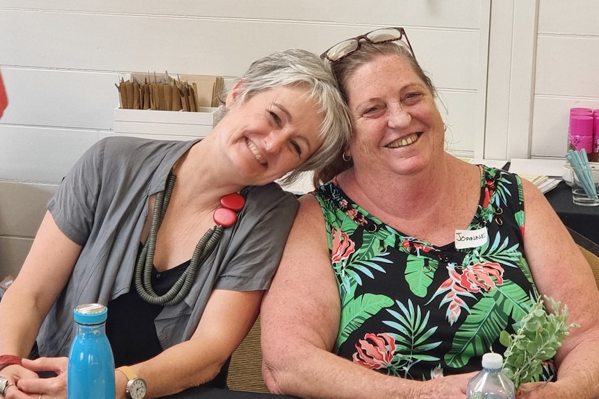 Two smiling women, one resting her head on the other's head.