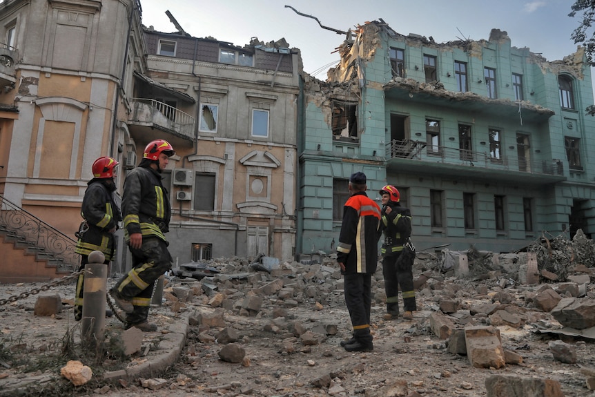 Rescuers stand on top of rubble in front of residential buildings damaged by missile strikes