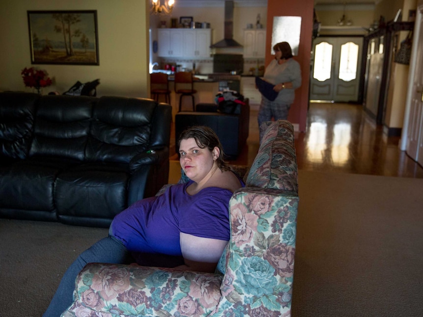 Jenna sits on the couch, while Sue folds up the washing.