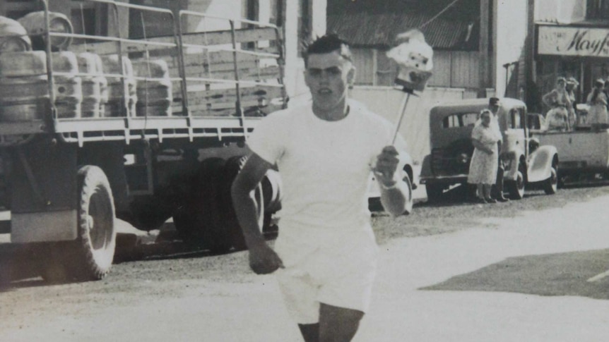 Man in white running in street with Olympic Torch