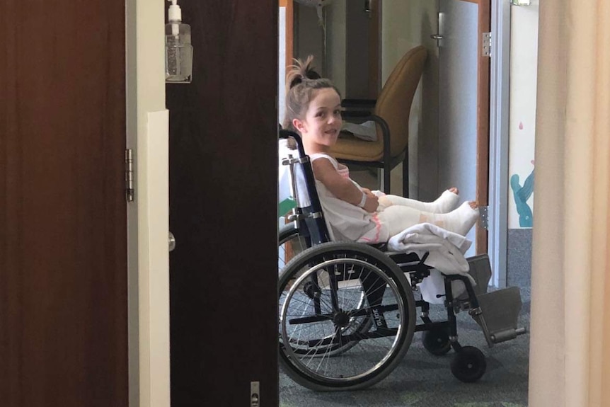 a young girl sitting in a wheelchair with both her legs wrapped in full length casts