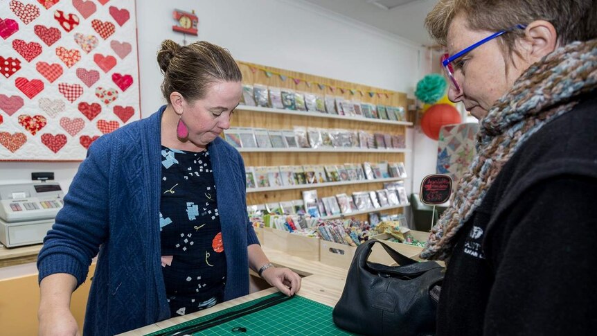 A woman and a shopkeeper measuring a zipper