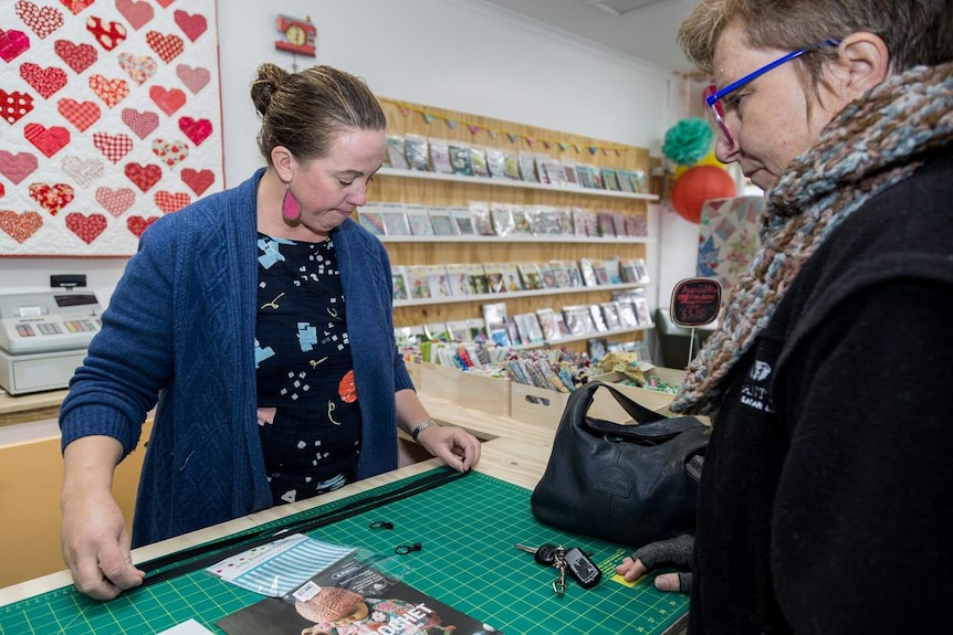 A woman and a shopkeeper measuring a zipper