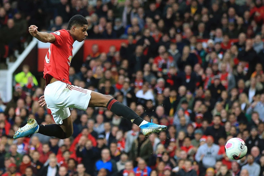 A Premier League striker extends his leg after shooting the ball in mid-air, scoring a goal.