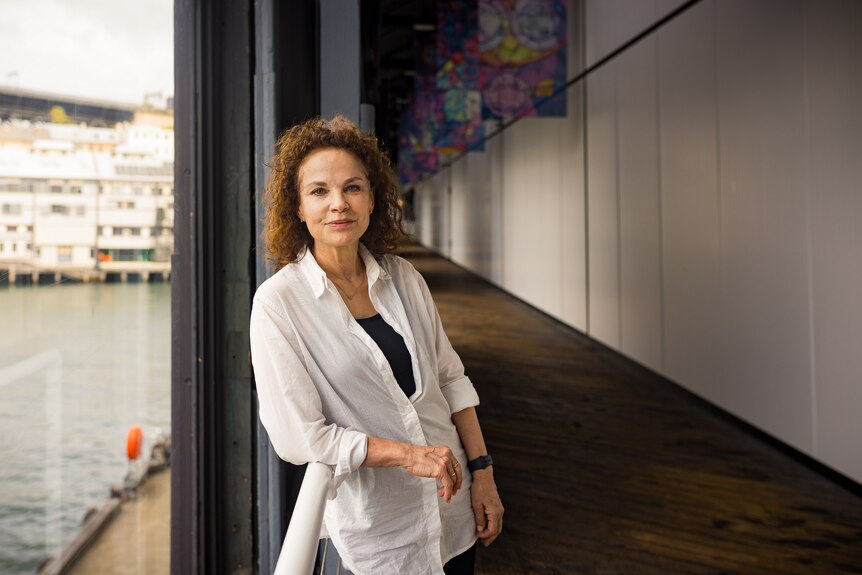 Sigrid Thornton, a 64-year-old white woman with curly brown hair wearing a white blouse and black pants leans against a railing.