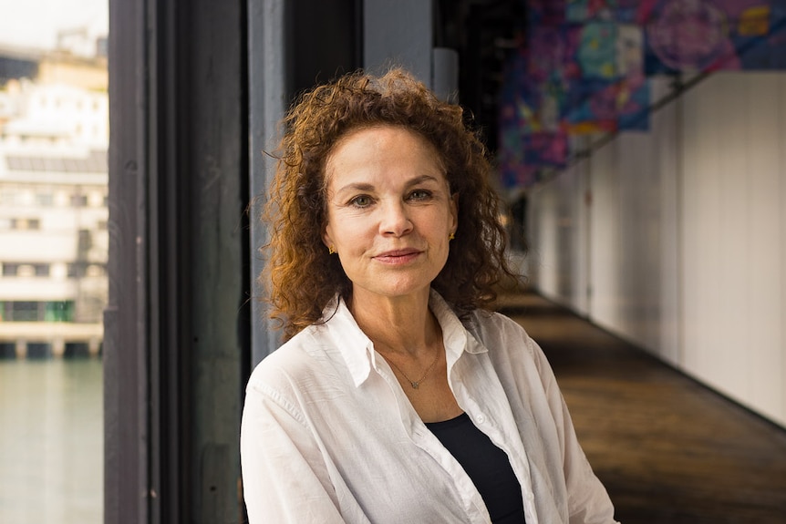 Sigrid Thornton, a 64-year-old white woman with curly brown hair wearing a white blouse and black pants leans against a railing.