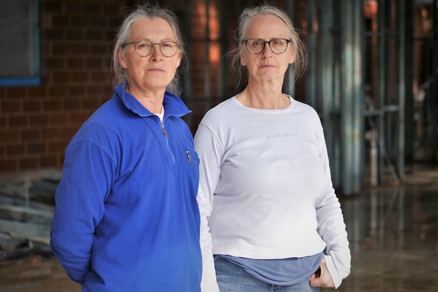 Two women standing next to each other inside the shell of their unfinished home