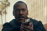 Eddie Murphy looking serious and pointing a gun with both hands, palm trees behind him