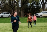 Women running in the foreground in dark activewear looking away from the camera. Three friends blurred in the background 