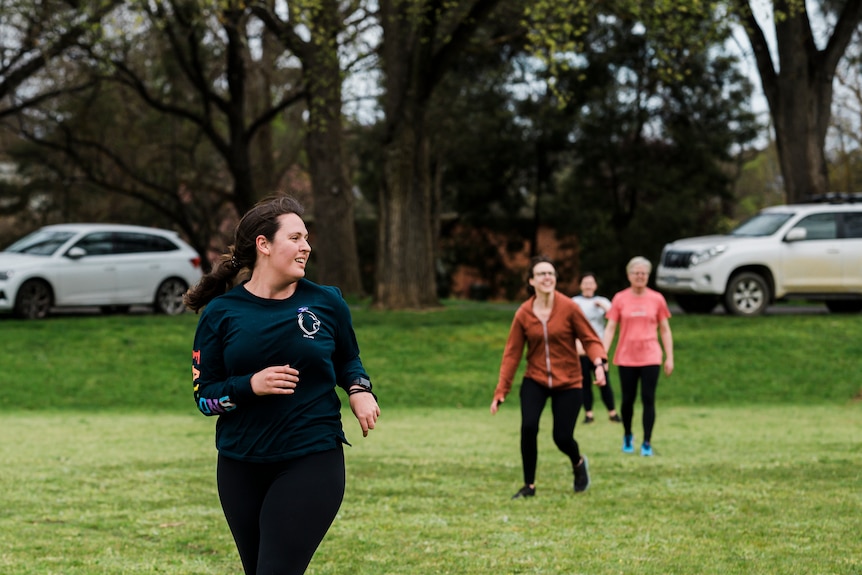 Women running in the foreground in dark activewear looking away from the camera. Three friends blurred in the background 