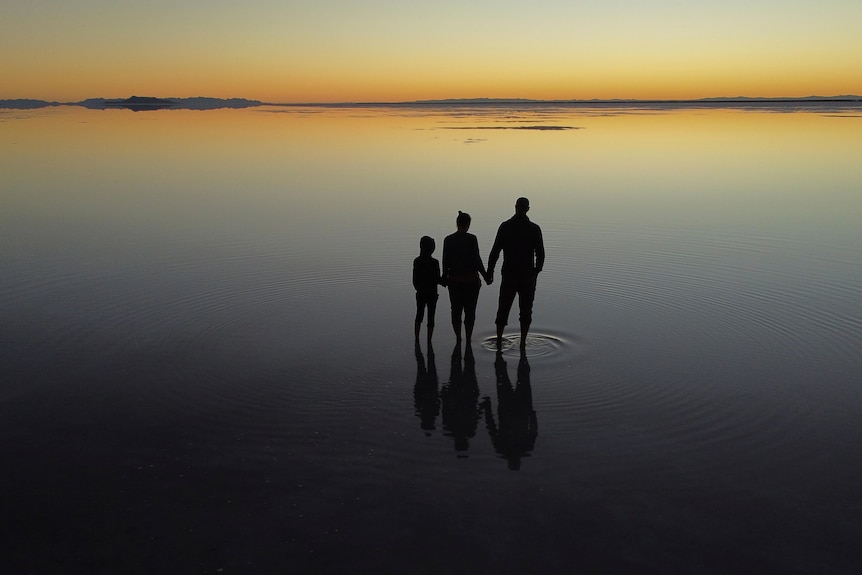 Three people standing in a lake as the sun rises