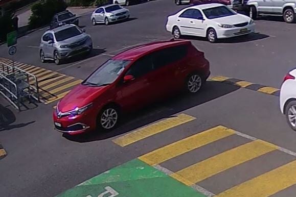 A red car is seen through security footage driving through a carpark.