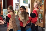 Three primary school-aged girls standing with possum skin cloaks over their shoulders