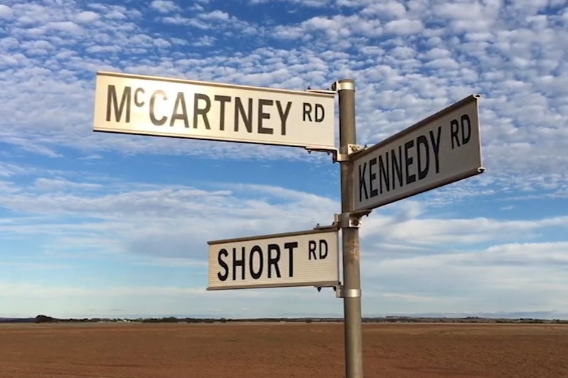 Three road signs point in different directions in country WA with a cloudy sky behind.