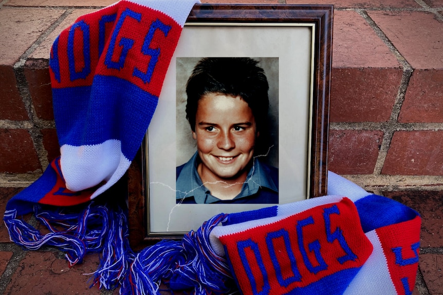 A photo of a young boy in a broken frame, draped in a Western Bulldogs scarf