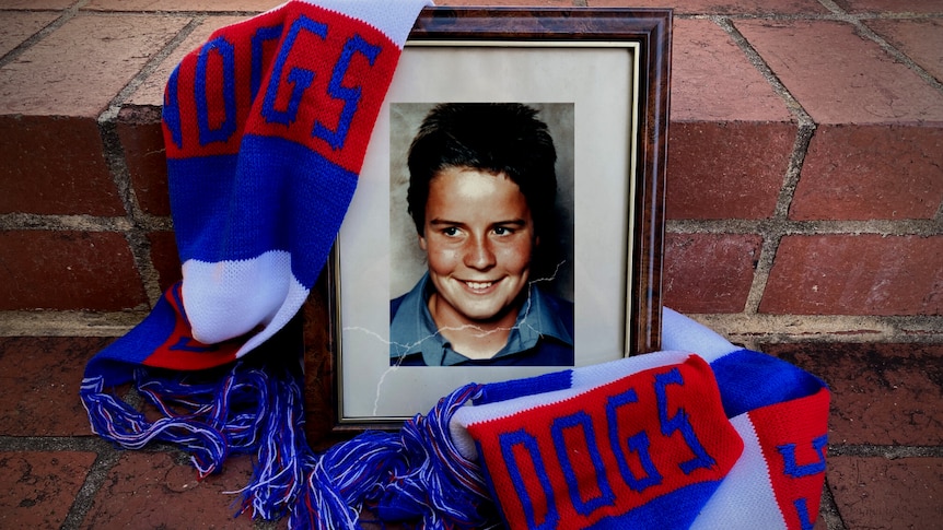 A photo of a young boy in a broken frame, draped in a Western Bulldogs scarf