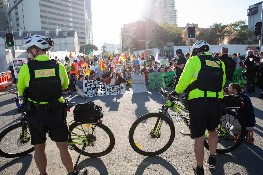 Protesters sit on Margaret Street and block traffic, watched by police.