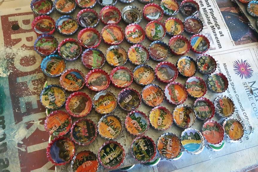 Close-up of lots of painted bottle caps drying on the bench.