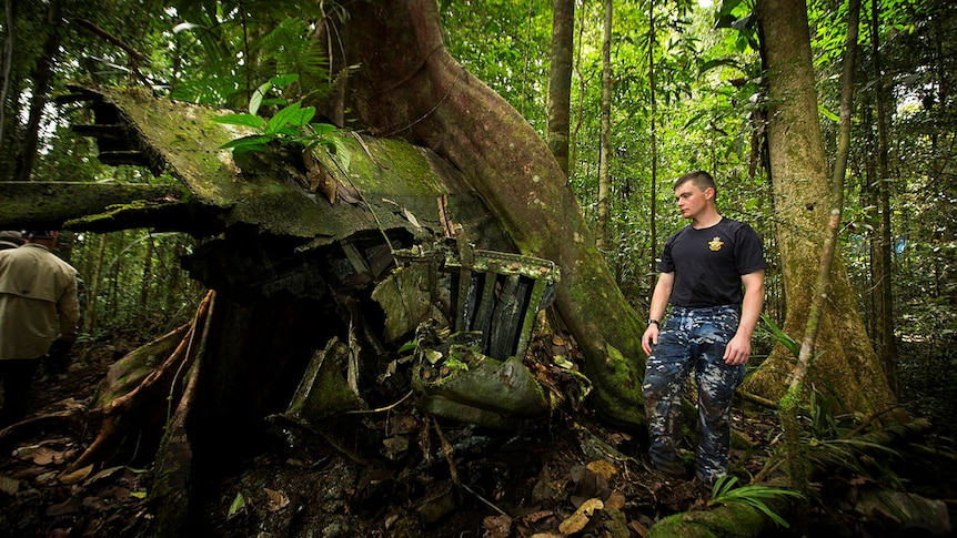 A young man in an Australian Defence Force uniform stands among the moss covered wreckage of the aircraft