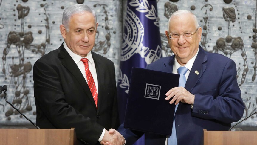 Israeli President Reuven Rivlin shakes hands with Israeli Prime Minister Benjamin Netanyahu as they stand behind a podium.