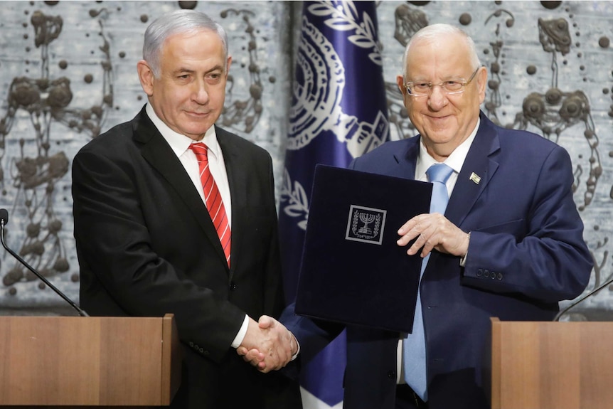Israeli President Reuven Rivlin shakes hands with Israeli Prime Minister Benjamin Netanyahu as they stand behind a podium.