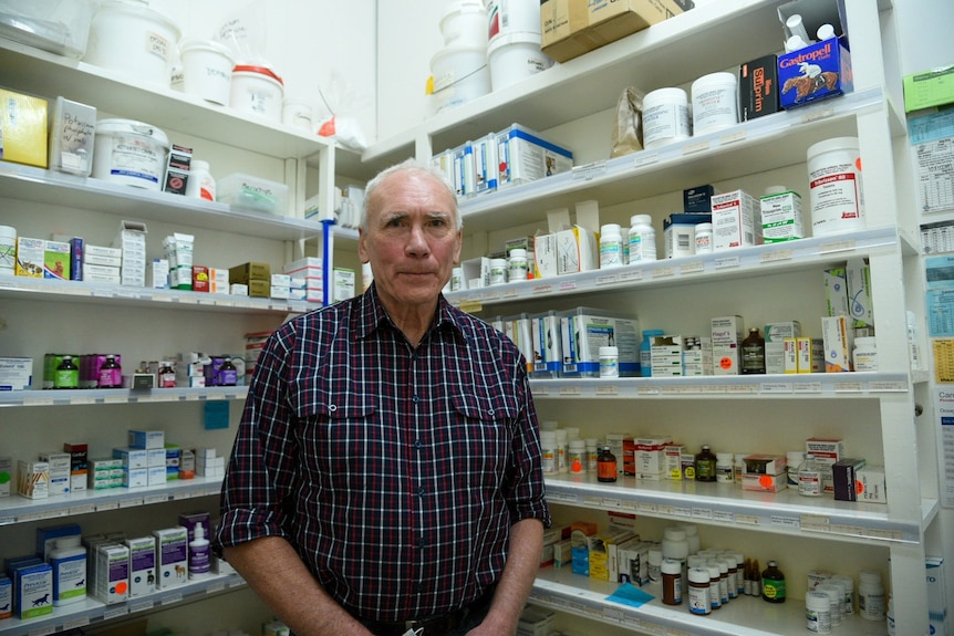 A man stands in front of shelves stacked with medication bottles.