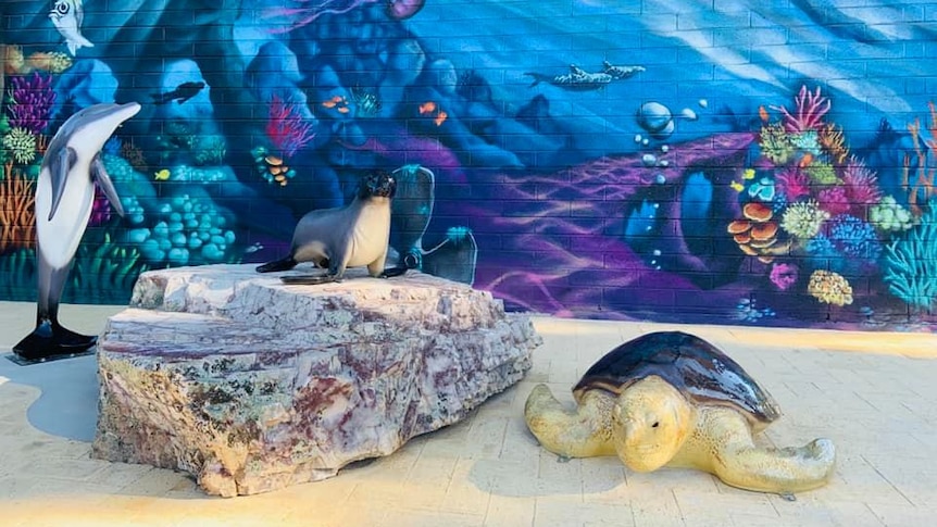 Statue of a dolphin, seal on a rock and a turtle in front of a wall with an underwater mural