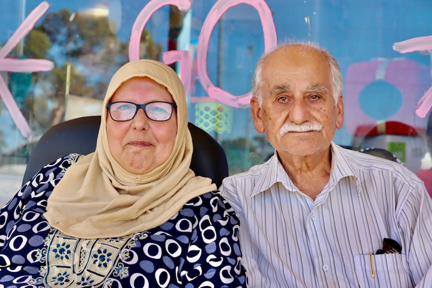 an old woman with a hijab and her husban posing in front of a shop's window