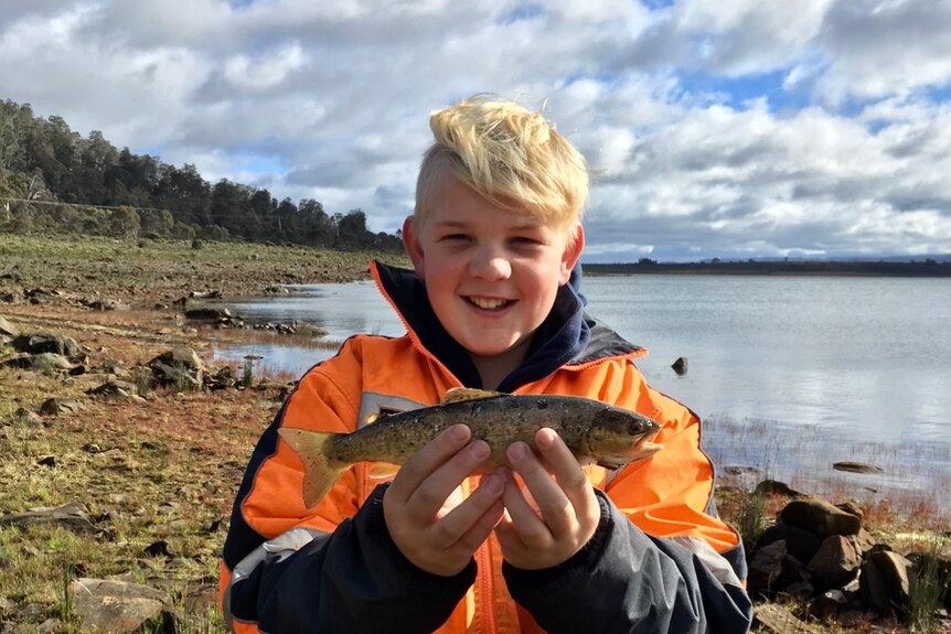 A young boy smiles as he holds a freshly caught fish. 