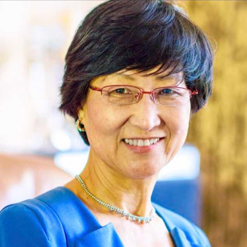 A woman wearing glasses with short black hair smiles at the camera.