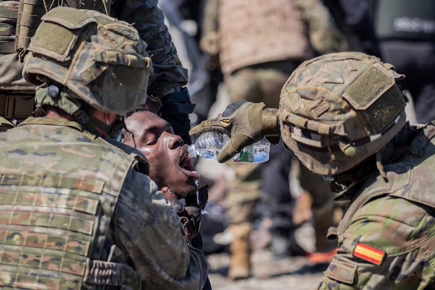 Spanish soldiers give a man water from a clear plastic bottle
